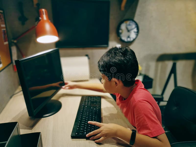 Asian Boy Wearing Red T-Shirt Using Computer in the Room. Cute Asian Boy Wearing Red T-Shirt Using Computer in the Room stock images