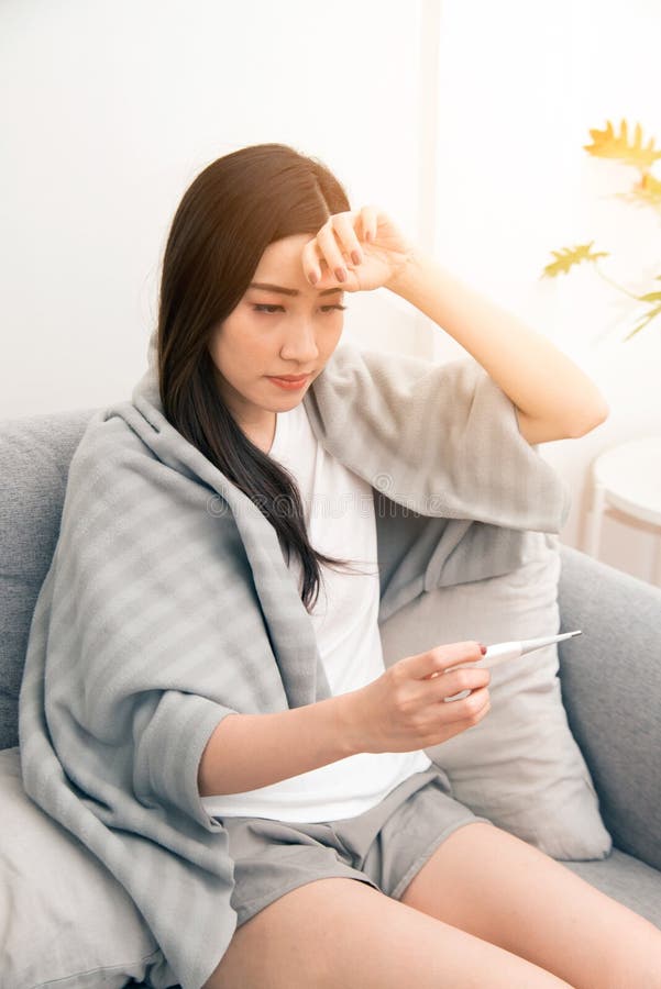 Asian woman sick from cold and used with thermometer suffering on sofa in the room royalty free stock photography