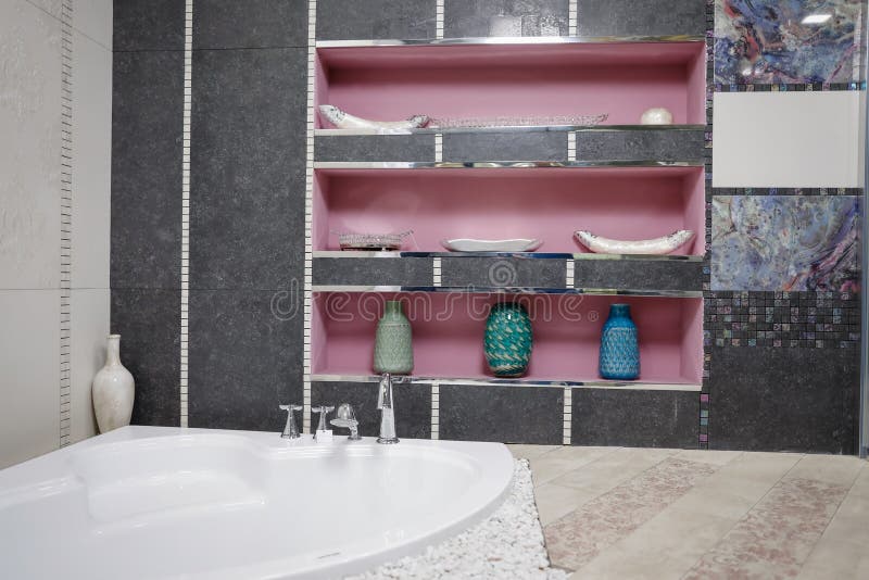 Bathroom with bathtub in the corner and three pink shelves in the back. On the walls are decorative,multi-colored mosaic. stock images