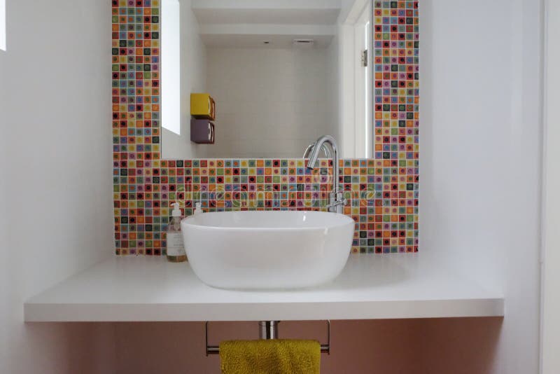 Bathroom wash basin with colorful glass mosaic tiles and mirror inset into the tiles. Bathroom ceramic wash basin with colorful hand made glass mosaic tiles and royalty free stock image