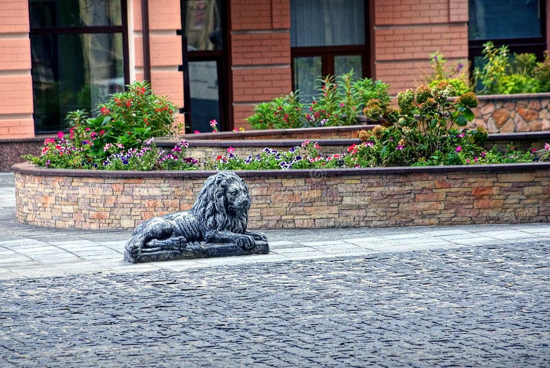 Iron decorative lion on the sidewalk and a flower bed in the yard. Beautiful scenery in the city courtyard near the buildings stock photo