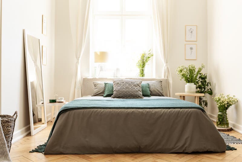 Beige, green and gray bedroom interior in a tenement house with a bed against a sunny window and bunches of wild flowers. Real pho stock photo