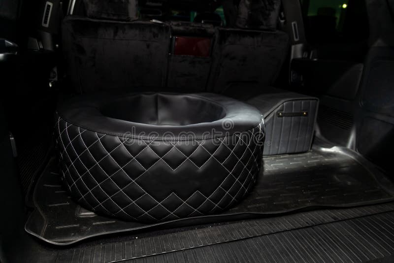 Car spare wheel sheathed in a black leather case and diamond-shaped stitching with white thread in the trunk of an SUV with a tool. Bag on a rubber mat. Auto stock image