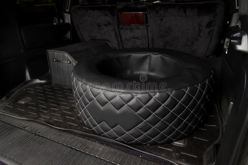 Car spare wheel sheathed in a black leather case and diamond-shaped stitching with white thread in the trunk of an SUV with a tool. Bag on a rubber mat. Auto royalty free stock images