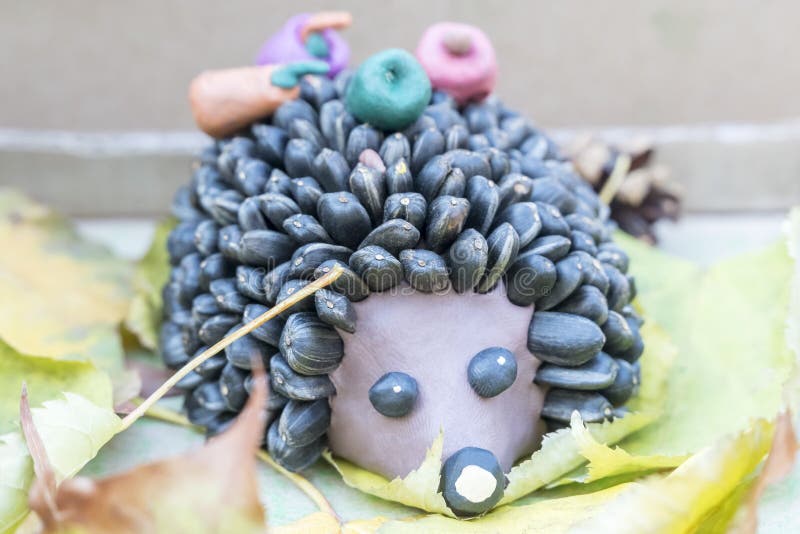 Children crafts - hedgehog from clay and seeds. Children crafts - hedgehog from plasticine and seeds instead of needles on autumn leaves stock photo