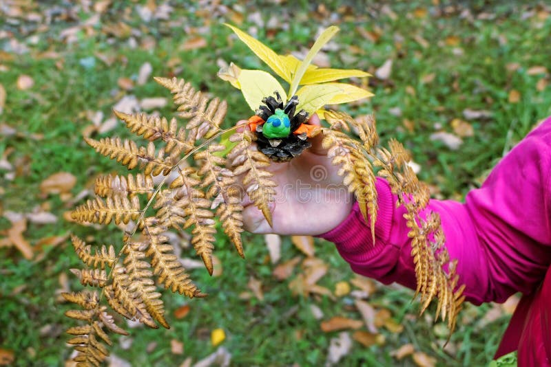 Children`s craft in the form of a hedgehog from a pine cone of autumn leaves and plasticine. Children`s creativity. The child`s hand holds a crafts made of pine royalty free stock photos