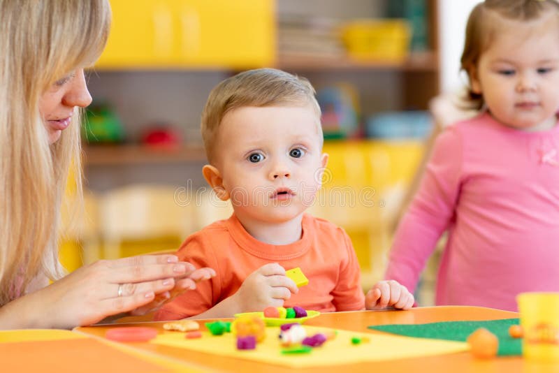 Children play with plasticine in kindergarten. Children with teacher play plasticine in kindergarten stock image