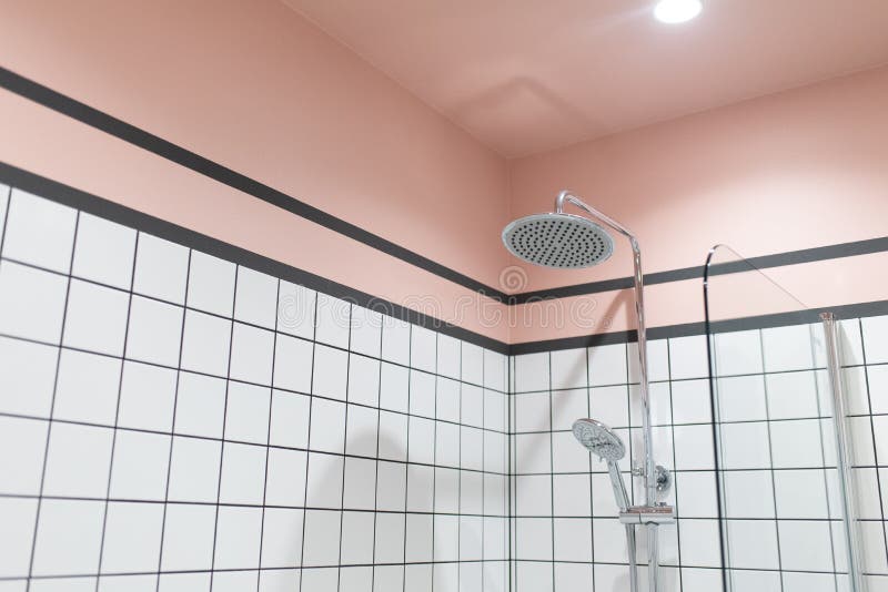 Closeup image of shower and shower head in a modern bathroom with white tiles and pink walls and ceiling stock image