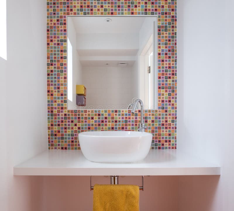 Contemporary bathroom with wash basin, colorful glass mosaic tiles, painted MDF shelf and mirror inset into the tiles. Contemporary bathroom with wash basin stock photo
