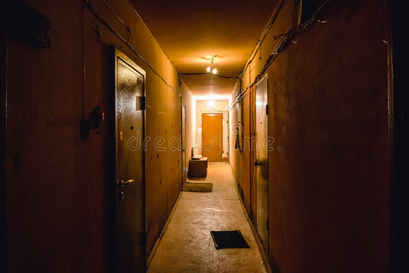 Dirty empty dark corridor in apartment building, doors, lighting lamps. Perspective, in yellow-orange tones, copy space royalty free stock photo
