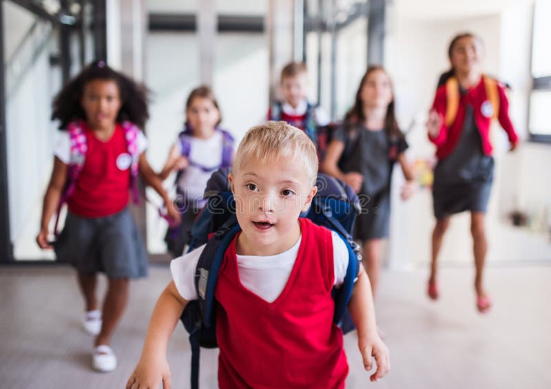 A down-syndrome school boy with group of children in corridor, running. A down-syndrome school boy with bag and group of children in corridor, running stock image