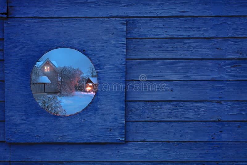 Fragment of a wooden fence with a round window. In the window is a beautiful winter night view of the village house. Toning stock images