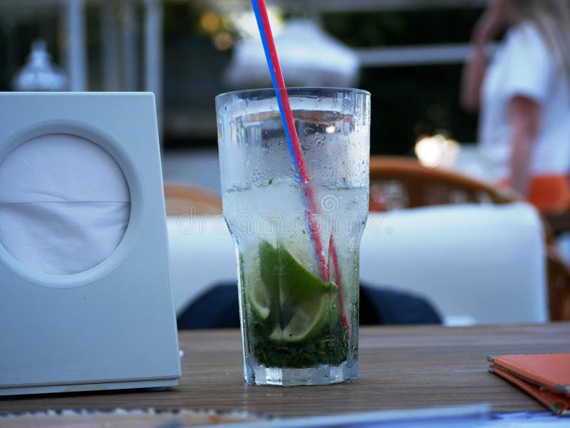 A glass of cold Mojito with ice is on the table on the summer veranda of the cafe. The glass with the tube is covered with droplet. S of condensate. Drink on a royalty free stock image