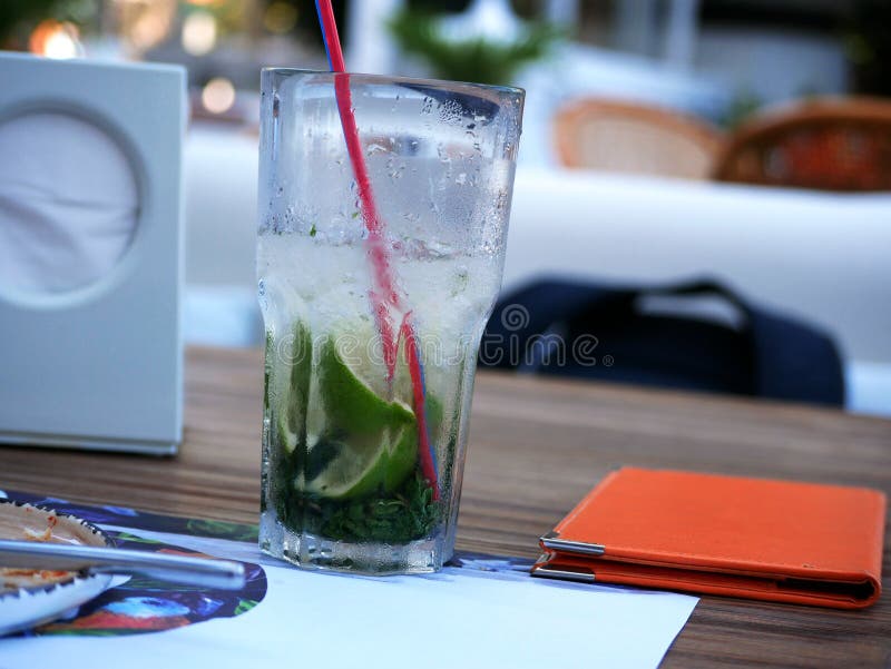 A glass of cold Mojito with ice is on the table on the summer veranda of the cafe. The glass with the tube is covered with droplet. S of condensate. Drink on a royalty free stock photo