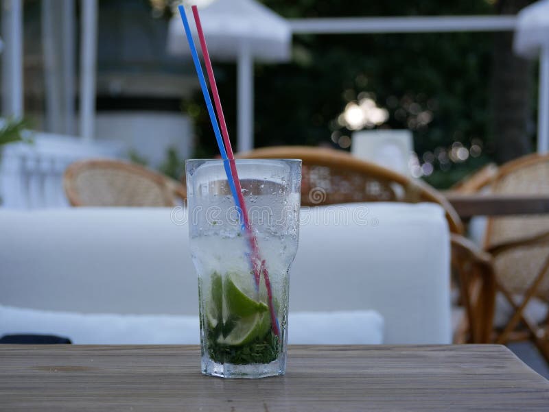 A glass of cold Mojito with ice is on the table on the summer veranda of the cafe. The glass with the tube is covered with droplet. S of condensate. Drink on a royalty free stock photography