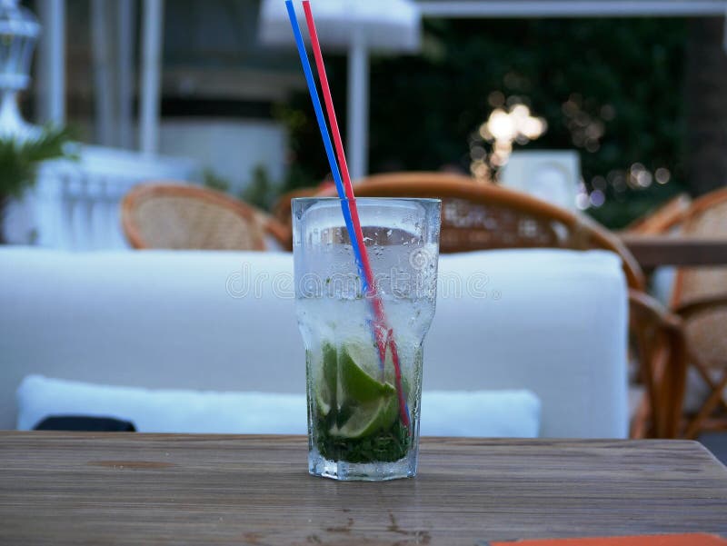 A glass of cold Mojito with ice is on the table on the summer veranda of the cafe. The glass with the tube is covered with droplet. S of condensate. Drink on a royalty free stock photography