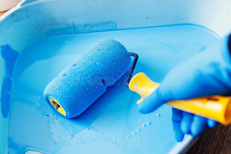 Gloved hand lowers the roller in the tray with blue paint. Services painter. Repair and decoration of apartments.  royalty free stock images