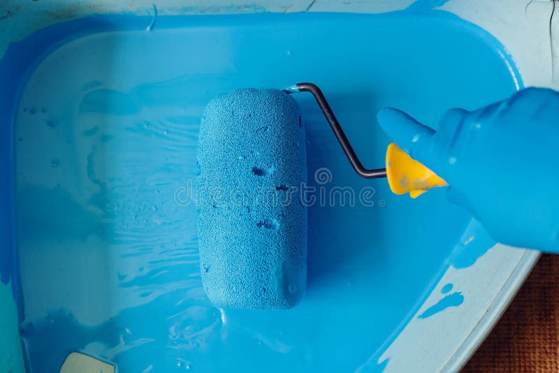 Gloved hand lowers the roller in the tray with blue paint. Services painter. Repair and decoration of apartments.  stock photos