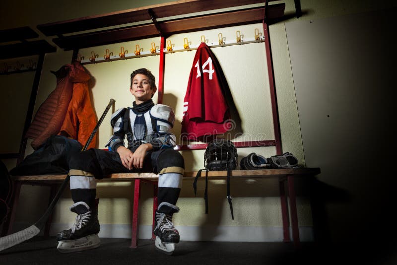 Happy boy sitting in ice hockey dressing room. Low-angle view of teenage boy, professional hockey player, sitting on the bench in the dressing room before the royalty free stock photography