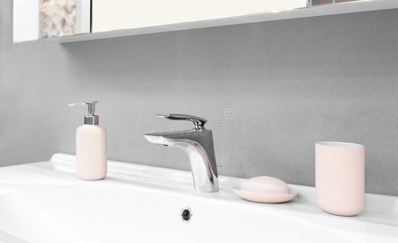 Luxury modern style faucet mixer on a white sink in a beautiful gray and white bathroom with pink glass accessories stock photography