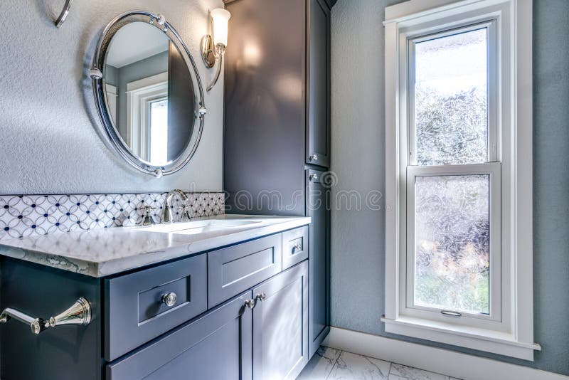 New blue bathroom design with mosaic accent tiles. New fresh bathroom with blue vanity, mosaic backsplash and a cabinet alongside marble floor stock photo