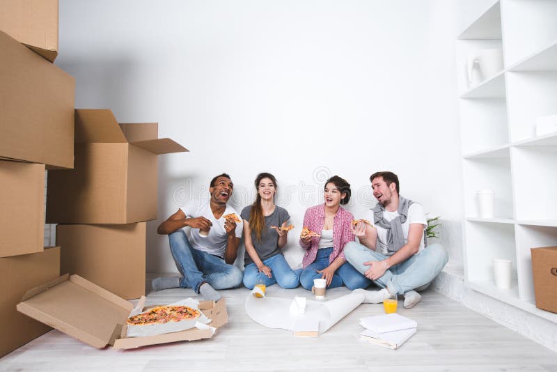 New home. Friends sitting on the floor in the new apartment and eating pizza after unpacking. Housewarming royalty free stock images