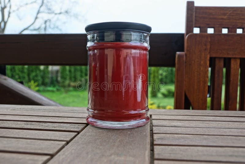 One red glass jar with a decorative candle stands on a brown board on the veranda. Against a background of green vegetation royalty free stock photo