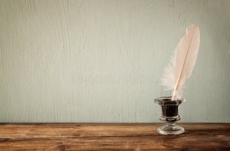 Photo of white Feather and inkwell on old wooden table. retro filtered image stock photo