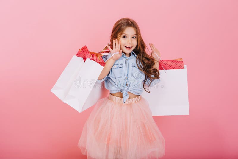 Pretty joyful young girl in tulle skirt, with long brunette hair walking with white packages on pink background. Lovely royalty free stock image