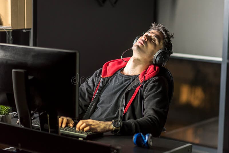Tired man working by computer in apartment. It is hard job. Calm young male demonstrating fatigue while typing on keyboard. He situating at desk in apartment stock images
