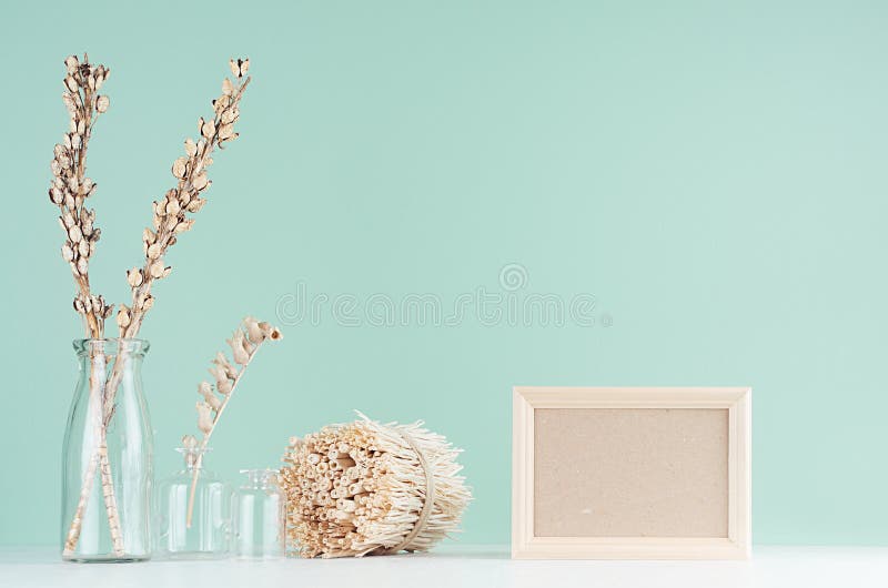 Traditional natural beige home decorations - dry flowers in transparent glass vases, twigs bunch, blank frame on green mint menthe. Wall, white table stock images