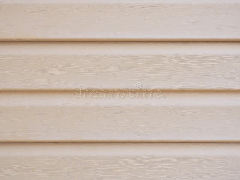 A wall of a house sheathed with plastic siding close-up. Light beige brown background or wallpaper. The material is faded and not. New. Reduced contrast royalty free stock images