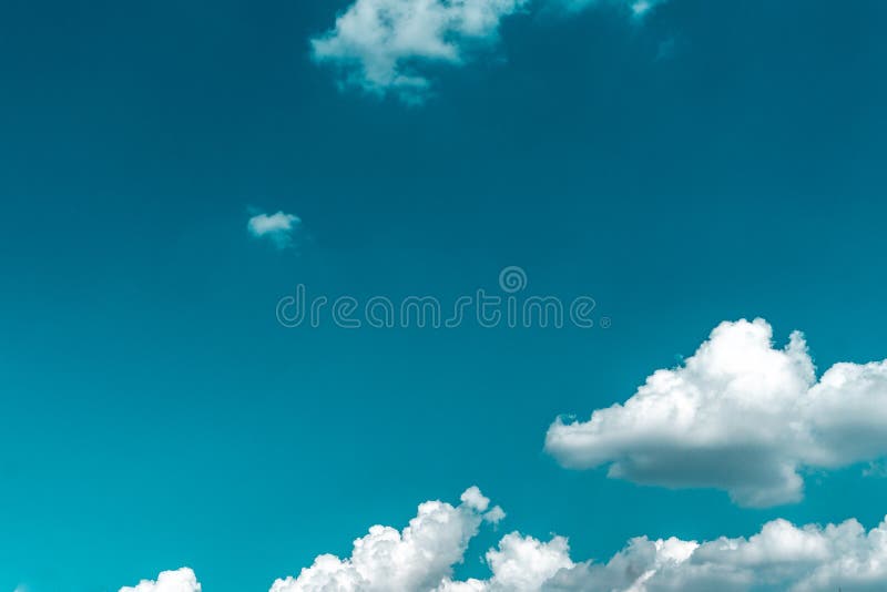White clouds with a gray bottom in the lower corner of the photo on a background of blue sky. The upper left corner is free of clouds. Horizontal orientation stock photography