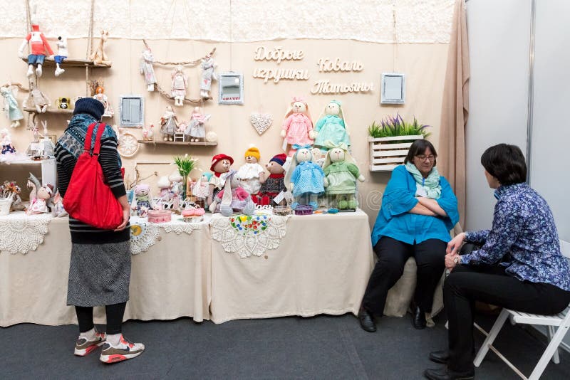 Woman stands at the booth with toys next to sitting needlewoman Tatyana Koval royalty free stock image