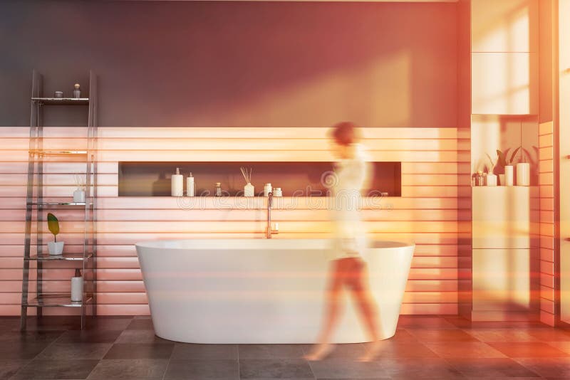 Woman walking in gray and pink bathroom with tub stock image
