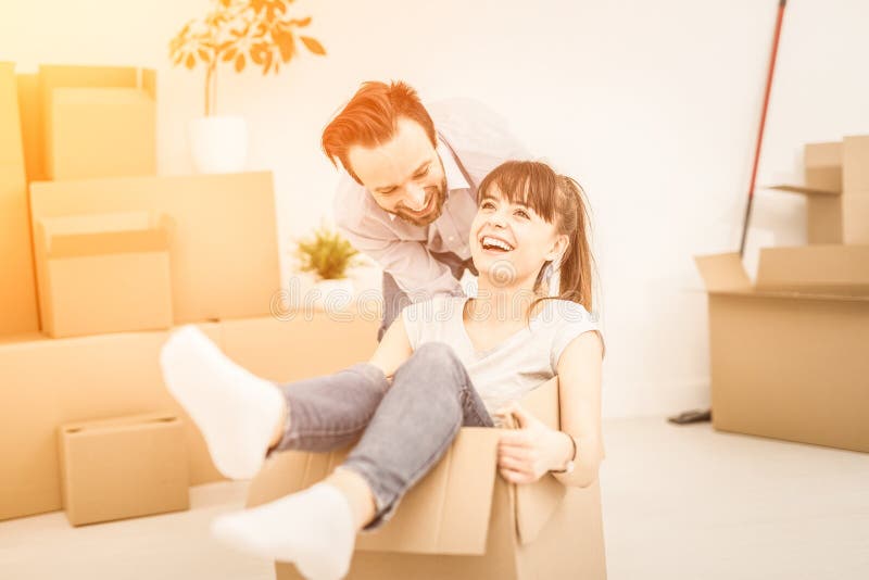 Young people move into a new apartment. Young couple people have fun while moving to a new apartment. Boy pushes box with the girl. Happy people in the new stock image