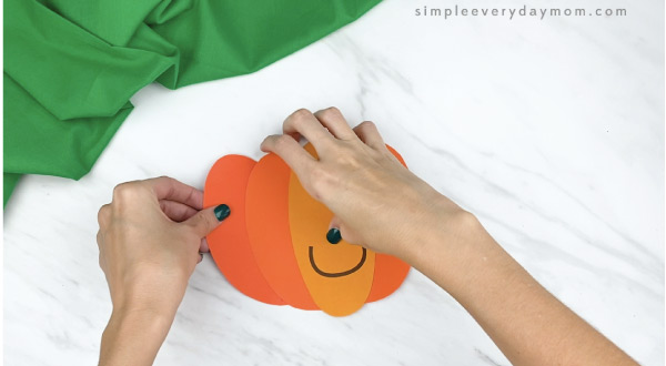 hands gluing paper pumpkin pieces together